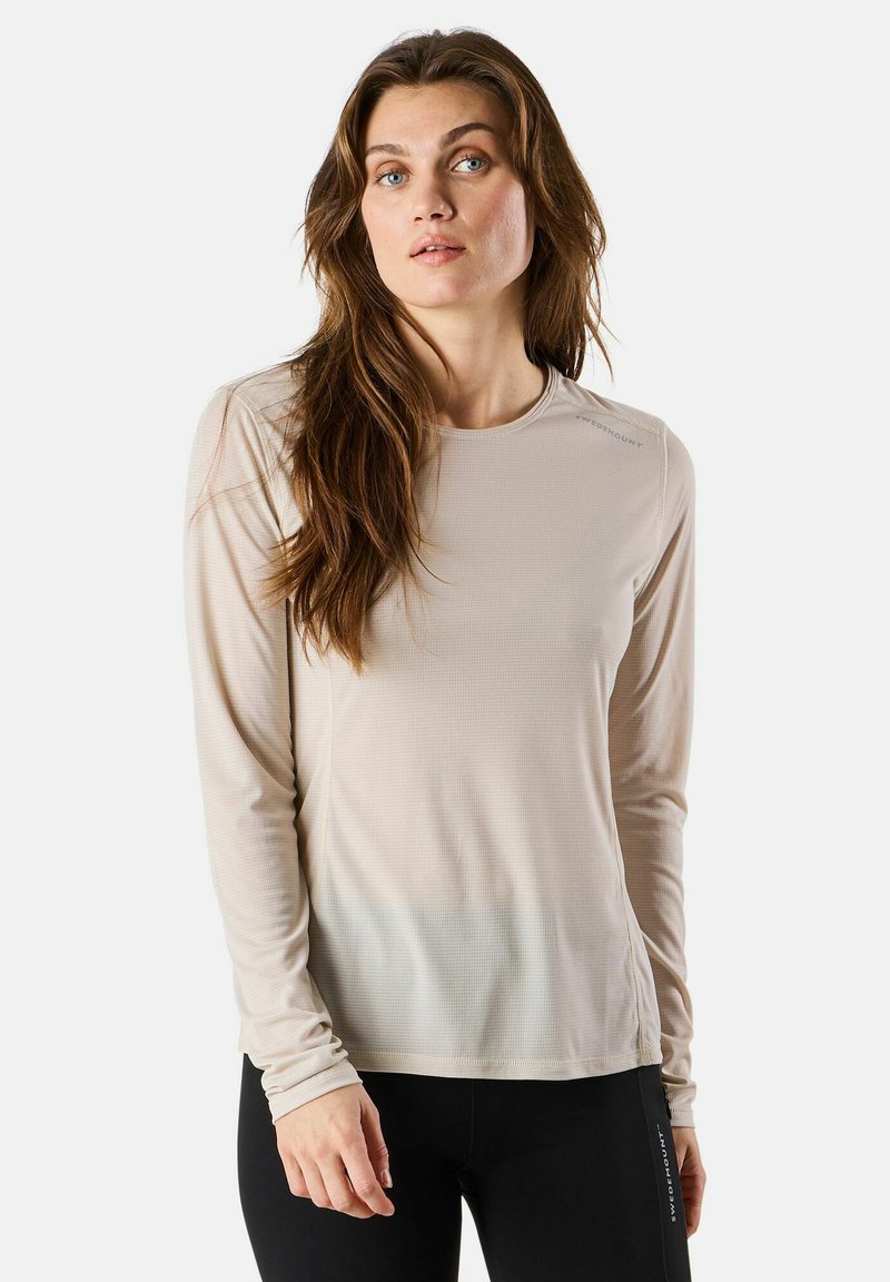 Lange mouwen sporttop in lichtbeige, met een textuurstof, naadloos ontwerp en een ronde halslijn, gecombineerd met zwarte leggings.