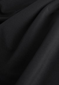 Gros plan sur un tissu noir lisse avec une texture diagonale fine et de légers plis créant des ombres et des reflets doux.