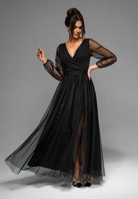 Abito da sera nero con scollatura a V profonda, maniche lunghe trasparenti e gonna in tulle fluente con uno spacco alto alla coscia e una fodera sottile.