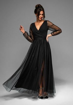 Black evening gown featuring a deep V-neck, sheer long sleeves, and a flowing tulle skirt with a thigh-high slit and subtle lining.