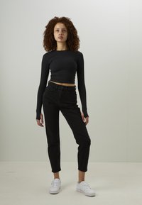 Μαύρο κοντομάνικο crop top με εφαρμοστή γραμμή, συνδυασμένο με ψηλόμεσα μαύρα τζιν και λευκά αθλητικά παπούτσια, τοποθετημένο σε ουδέτερο φόντο.