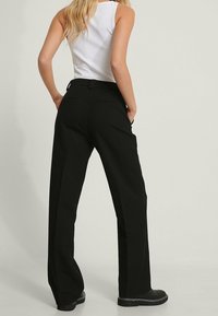 Wide-leg black trousers made of a smooth material, featuring a waistband and back pockets. Styled with a white tank top and black shoes.