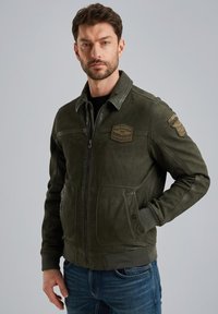 Chaqueta bomber de cuero verde oscuro con cierre de cremallera, puños acanalados y dos bolsillos delanteros, con parches en relieve en el pecho y la manga.