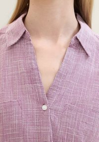 Camisa ligera de cuadros en burdeos y blanco, con cuello y un cierre de un solo botón en el pecho. Tejido texturizado.