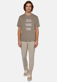 Šedé tričko s krátkým rukávem a bílým nápisem "TECH YOUR TIME," kombinované s béžovými kalhotami a světlými teniskami, stojící na bílém pozadí.