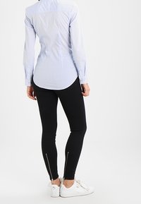 Lysblå stribet langærmet skjorte med rundet kant, parret med sorte leggings med lynlåsdetaljer ved anklerne, og hvide sneakers.