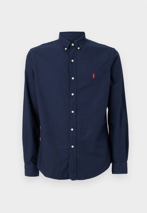 Marineblå skjorte med knapper laget av bomull, med klassisk krage, lange ermer og en liten rød logo på venstre bryst.