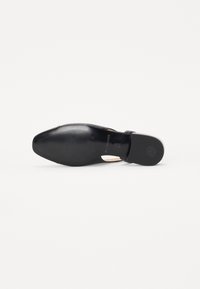Chaussure noire à bout pointu et à talon fin, avec un dessus en cuir lisse et une semelle en caoutchouc texturé. Design découpé près de la cheville.