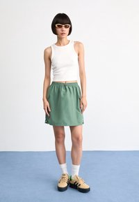 Green, elastic-waist skirt with side pockets, paired with a white fitted tank top and beige sneakers. Sunglasses complete the look.