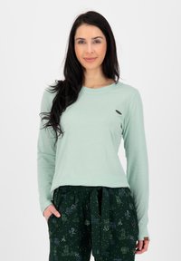 Lichtgroene langsloven shirt met een ronde halslijn, voorzien van een klein logo-accent. Gecombineerd met donkergroene gebloemde broek.