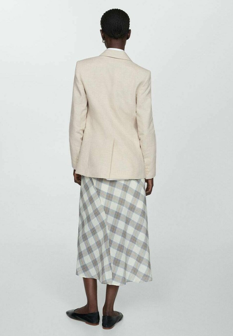 Beiger Leinen-Blazer mit einem einzelnen Rückenschlitz, getragen über einem langen, karierten Rock in Blau, Grau und Weiß. Schwarze Ballerinas runden das Outfit ab.