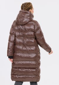Brun oppustet frakke med en blank finish, oversized hætte og syede paneler. Lange ærmer og en knælang design.