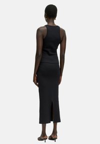 Zwarte geribbelde tanktop gecombineerd met een bijpassende midi-rok, voorzien van een split aan de achterkant voor gemakkelijke beweging. Glad materiaal met een getailleerde pasvorm.
