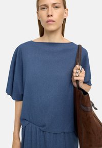 Niebieska teksturowana bluzka z dekoltem łódkowym i luźnymi rękawami, zestawiona z brązową torebką z zamszu z skórzanymi akcentami.