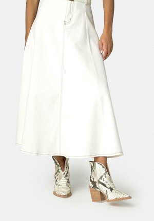 Mujer con falda midi blanca de línea A y botines blancos con estampado de piel de serpiente y tacones gruesos.