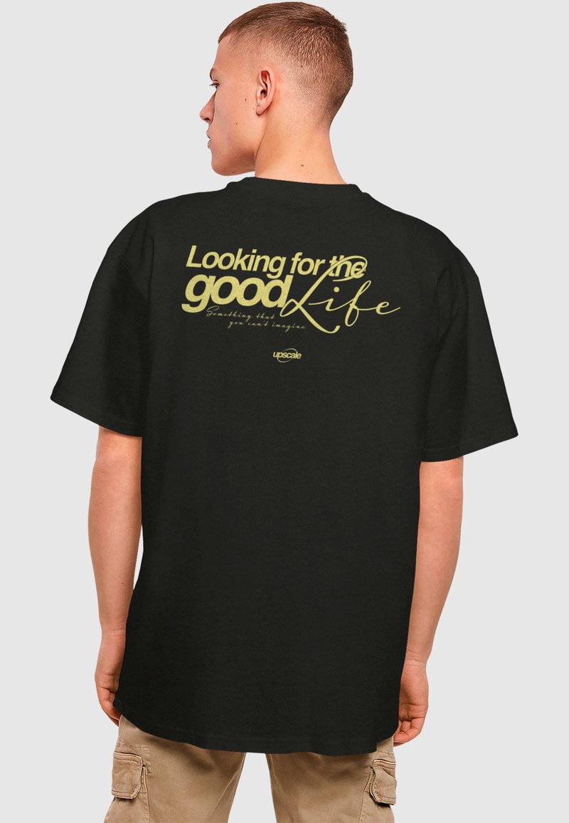 T-shirt en coton noir avec un grand texte jaune au dos qui dit "À la recherche de la belle vie" avec une calligraphie et un logo.