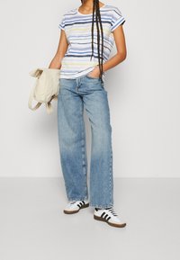 Pruhované tričko v bílé, modré a žluté; v kombinaci s vysokým pasem, širokými světle modrými džíny; modelka drží béžovou tašku; má na sobě bílé tenisky.