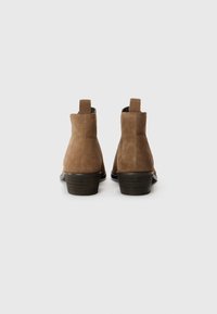 Botas de tobillo de ante marrón con un leve tacón, que presentan una textura suave, tiradores en la parte posterior y un diseño de punta redonda.