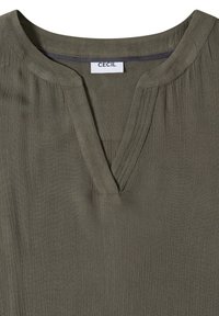 Blouse en tissu texturé vert olive avec un col en V et une étiquette de marque "CECIL" visible à l'intérieur du col.