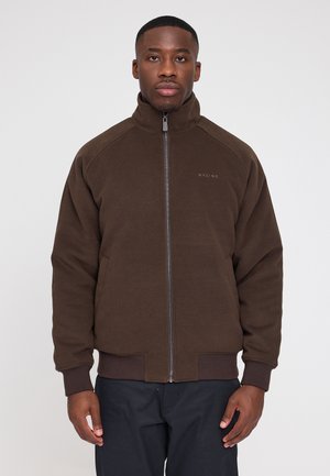 Brown zip-up jacket with a high collar, soft fabric, ribbed cuffs and hem, featuring a logo on the left chest, worn by a model.