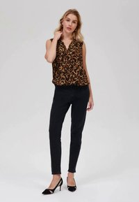Blusa senza maniche con stampa leopardata in marrone e nero, abbinata a jeans skinny neri e tacchi a punta neri con accenti neutri.