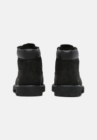 Bottines noires en cuir suédé avec un col en cuir lisse. Semelle en caoutchouc cranté, coutures renforcées et logo minimal.
