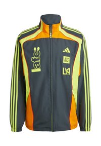 Trainingsjack in donkergrijs met gele en oranje accenten. Voorzien van een hoge kraag, ritssluiting aan de voorkant en drie-strepen ontwerp op de mouwen. Inclusief logo's.