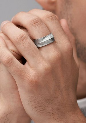Silver ring with a twisted design featuring textured grooves, displayed on a hand with natural skin tone and visible fine hairs.