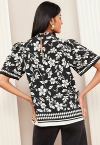 Must mustriga must valge lillemustriga, lühikesed puff-sleeved varrukad ja uksekujulise selja detailiga. Geomeetriline ääris hemline'il lisab visuaalset huvi.