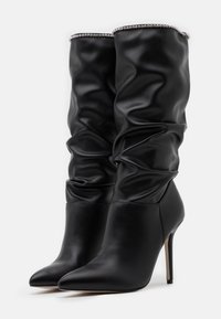 Botas negras hasta la rodilla confeccionadas en cuero liso, con un diseño fruncido, punta puntiaguda y tacón de aguja, adornadas con un acento de cristales.