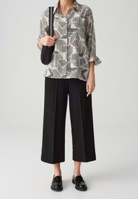 Blouse à motifs ondulés noirs et blancs, associée à un pantalon large noir taille haute et des mocassins noirs. Comprend un petit sac noir.