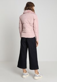 Veste rose gonflée avec un col en fourrure, dotée de coutures horizontales. Portée avec un pantalon large noir et des baskets gris clair.