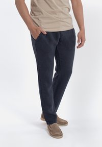 Navyblauwe linnen broek met een relaxte pasvorm, voorzien van zijzakken en een licht taps toelopend ontwerp. Gecombineerd met beige schoenen.