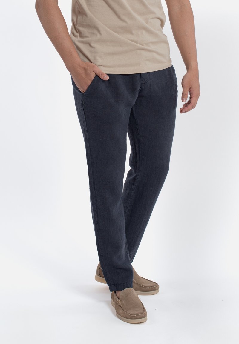 Navyblauwe linnen broek met een relaxte pasvorm, voorzien van zijzakken en een licht taps toelopend ontwerp. Gecombineerd met beige schoenen.