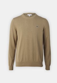 Beige knit sweater featuring a crew neck, ribbed cuffs and hem, with a small green Lacoste logo on the chest. Soft texture, casual design.