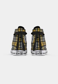 Geltonai ir pilkai raštuoti Converse All Star aukšti sportbačiai su juodomis kaspinu raišteliais, matomi iš nugaros.