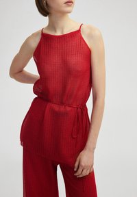 Top de punto rojo con tirantes finos y corte holgado, que presenta un patrón texturizado y un detalle de cintura atada.