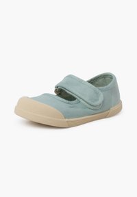 Zapatilla de lona azul claro con punta redondeada, correa de velcro y suela de goma texturizada. Diseño minimalista con acentos en beige contrastantes.