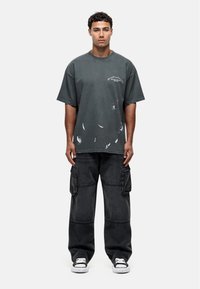 Overdreven donkergrijze t-shirt met versleten details, ronde hals, gecombineerd met losse zwarte cargobroek met zijzakken en contrasterende stiksels.