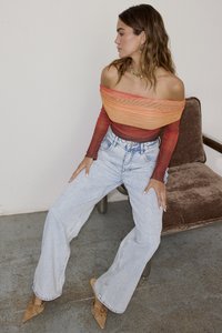 Off-shoulder gradient topp i oransje til rødt, kombinert med lyseblå vide jeans og beige spisse sko. Enkle smykker som tilbehør.