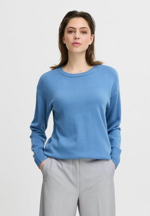 Pull en tricot bleu clair avec un col rond, des manches longues et des poignets côtelés, associé à un pantalon gris clair. Texture lisse.