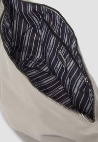Sac beige ouvert montrant une doublure intérieure à rayures noires et blanches avec des logos "S. Oliver" et une poche intérieure zippée.