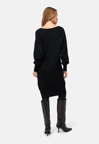Czarna dzianinowa sukienka swetrowa z okrągłym dekoltem i bufiastymi rękawami, w zestawieniu z połyskującymi, czarnymi kozakami za kolano. Prosty i minimalistyczny design.
