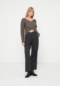 Brun crossover strikkegenser med lange ermer, kombinert med høyt midje, vide grå bukser med knappdetalj og svarte ankelstøvler.