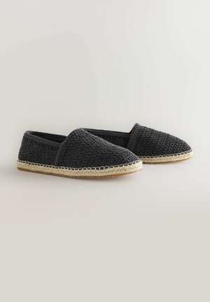 Melnas austas slip-on kurpes ar faktūru augšdaļu, ar jutu zoli un šuvju detaļām malā. Plakans, ikdienišķs dizains.