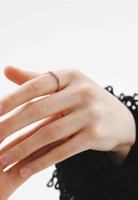 Anillo de banda retorcida de plata llevado en una mano de piel clara. Textura suave, diseño minimalista, sin adornos ni patrones adicionales.