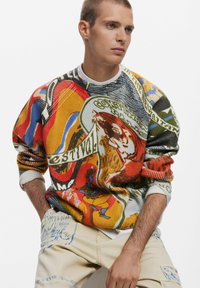 Farverig strikket sweater med en blanding af abstrakte mønstre i rød, gul, blå og grøn. Ribbet manchetter og rundt halsdesign; tekstureret stof.