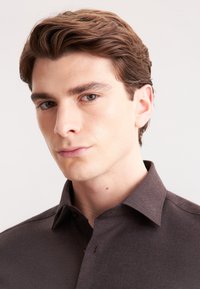Camicia marrone con bottoni, caratterizzata da un colletto classico e un tessuto texturizzato. Il primo piano mostra la vestibilità, i dettagli e la finitura liscia.