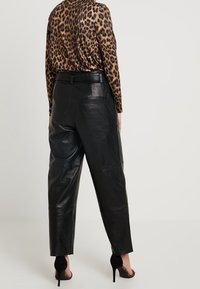 Zwarte leren broek met een losse pasvorm, met een gladde textuur en twee achterzakken. Gecombineerd met een top met luipaardprint.