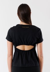 T-shirt nera in cotone con maniche corte, caratterizzata da un design arricciato sul retro e un'apertura a taglio. Logo "Patrizia Pepe" in borchie metalliche sul collo.